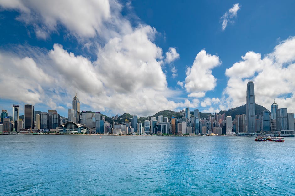 Breathtaking view of Hong Kong skyline across Victoria Harbour under a vibrant blue sky.