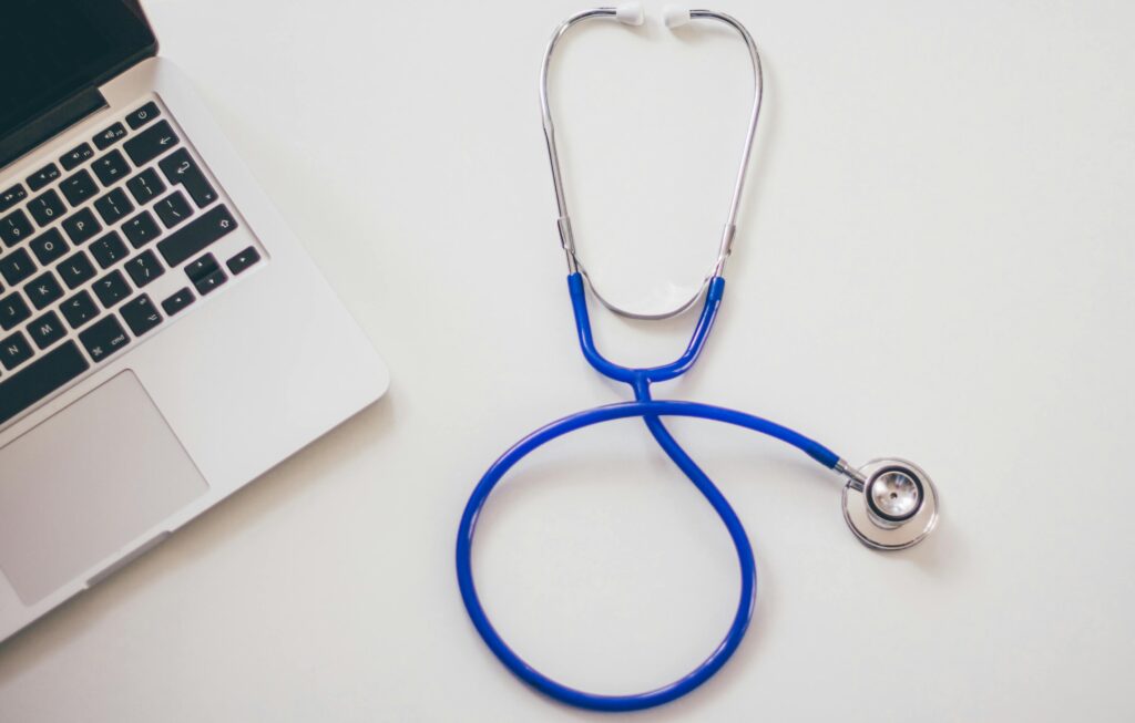 Medical stethoscope and laptop on a white desk, symbolizing digital health solutions.