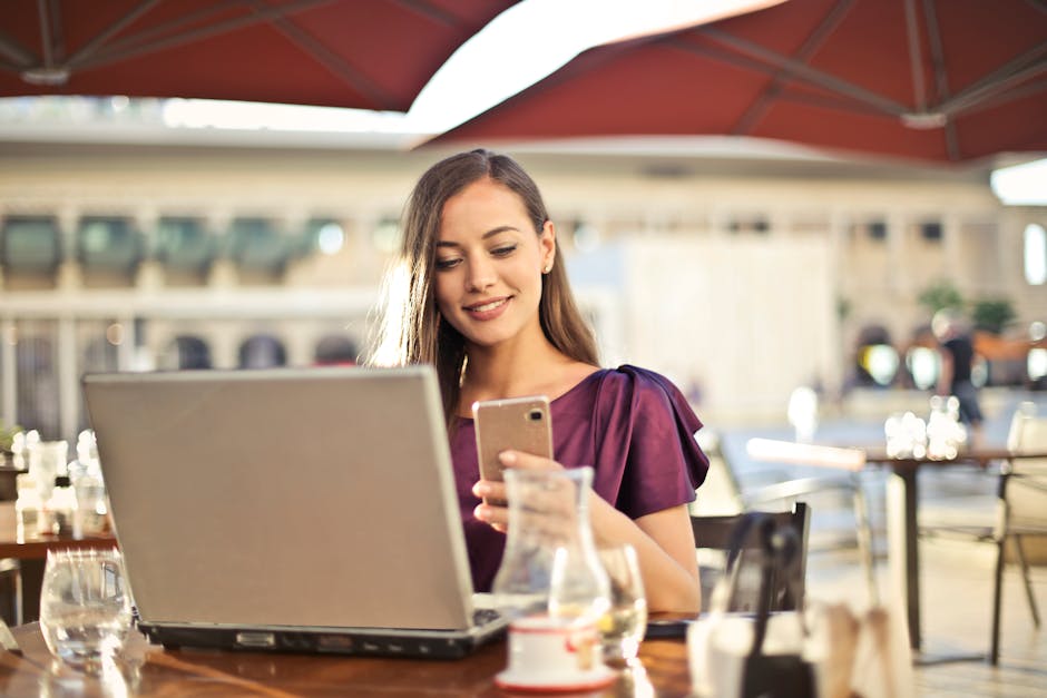 Woman enjoying remote work at a café, using a laptop and smartphone.